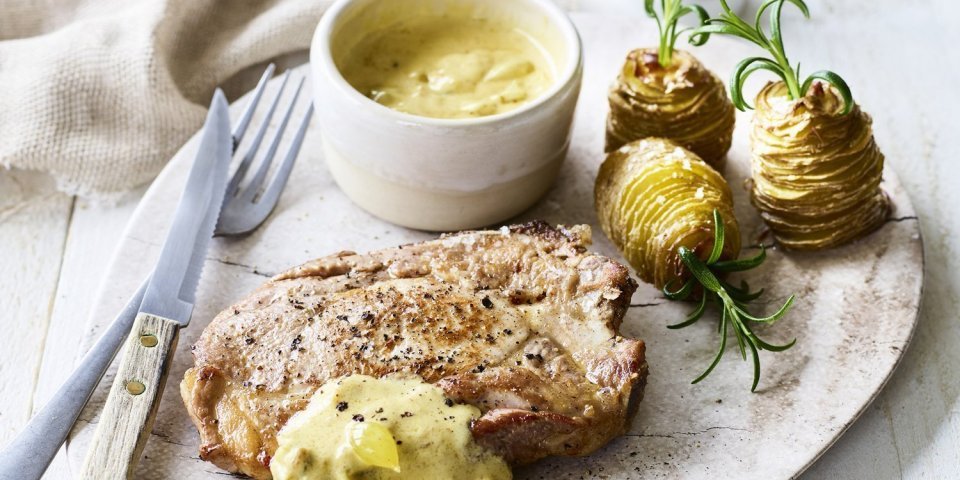Spieringkotelet met picklessaus en aardappeltorentjes Een bordje om meteen aan te vallen! Een sappige varkenskotelet met picklessaus en aardappeltorentjes met verse rozemarijn. Het bestek ligt langs het bordje, bovenaan een witte pepermolen en servette.