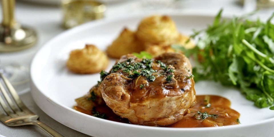 Stoofpotje met varkensvlees en pomme duchesse van pastinaakpuree Het hoofdgerecht is geserveerd op een wit groot bord. Ieder krijgt een portie schenkel, pommes duchesse en frisse rucolasla.