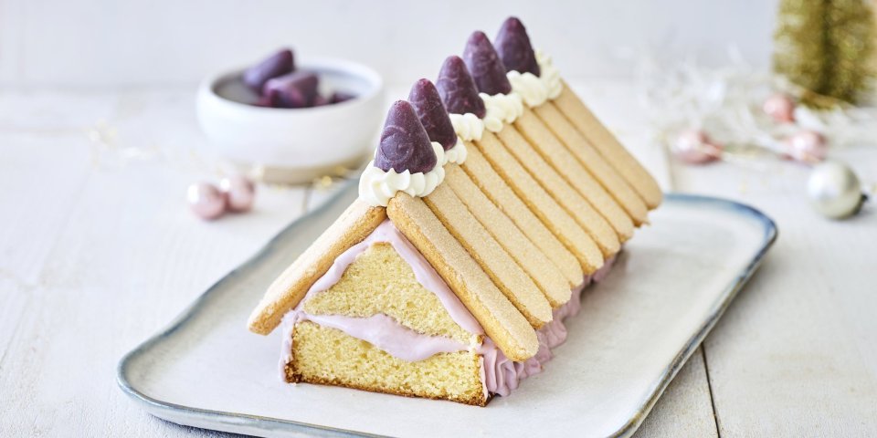 Taart kersthuisje met cuberdon Op een schaaltje staat een taart in de vorm van een kersthuisje gemaakt uit een cake met lange vingers en cuberdons. De cake is de vorm van het huis en hierop werden de lange vingers gelegd als dakplaten. De cuberdons staan in een toefje slagroom hier bovenop.