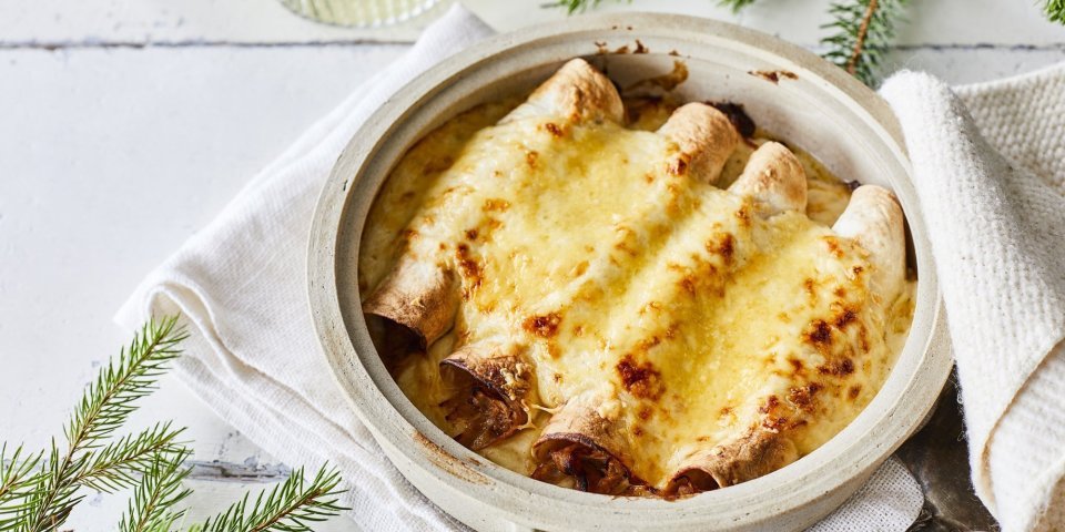 Opgerolde wraps gevuld met traagggegaard vlees liggen netjes naast elkaar in een ovenschotel. Hierover is kaassaus geserverveerd en even gegrild. Perfecte snack als bijgerechtje op je feesttafel, heerlijk voor groot en klein. 