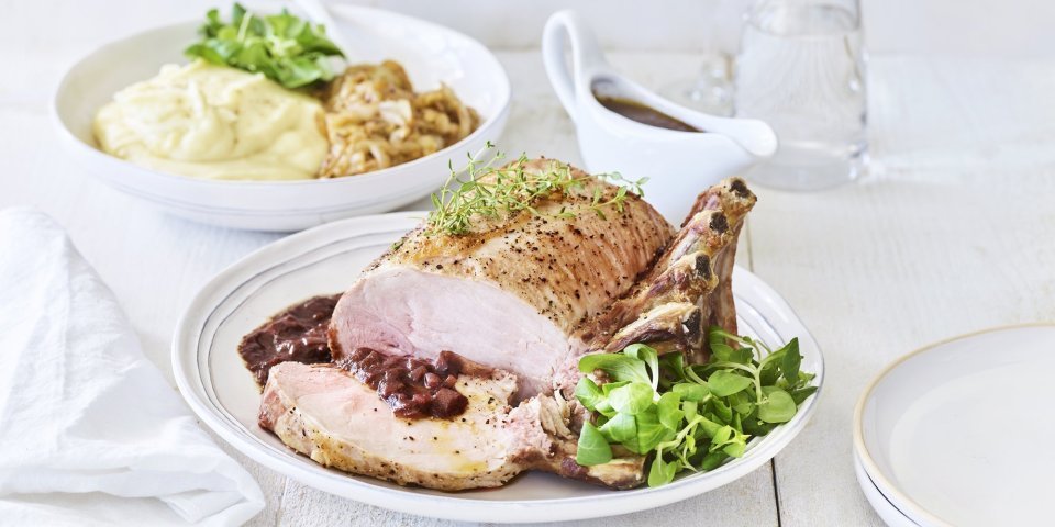 Varkenskroontje met puree, Pas de Rouge-kaas en witloof Een varkenskroontje ligt op een groot wit bord, aangesneden en opgediend met de rode wijn saus. In de achtergrond staat de aardappelpuree en de stukjes witloof. Het varkensvlees is mooi roos gebakken.
