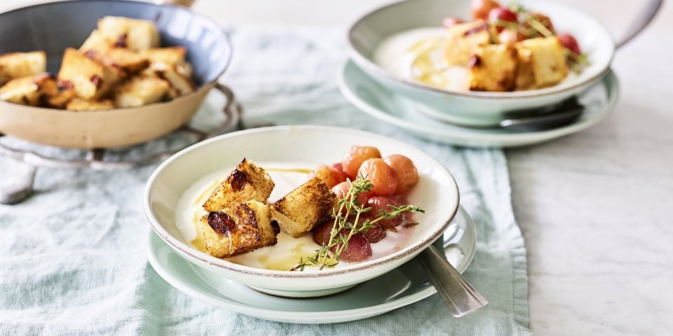Yoghurt met gegrilde druiven en croutons Een heerlijk én makkelijk ontbijtje staat klaar op tafel. De yoghurt is geserveerd in ontbijtkommetjes en afgewerkt met gegrilde druiven en krokante croutons van rozijnenbrood.