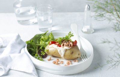 Een gepofte aardappel feestelijk afgewerkt met zure room, garnaaltjes en kerstomaatjes. Het gerechtje is afgewerkt met een groene salade dat instant kleur geeft aan het gerecht. 