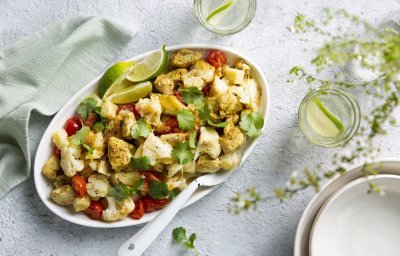 Aloo gobi is een Indiase curry van aardappel en bloemkool. Wij deden er nog stukjes kip bij. Deze rijkgevulde schotel van groenten en kruiden staat op tafel met een grote witte lepel bij. Voor de afwerking werd deze schotel gepresenteerd met korianderblaadjes en limoenpartjes. 