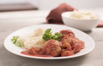 Eén portie balletjes in tomatensaus met puree, komt eraan. Hij staat klaar op een houten tafel, klaar om op te eten.