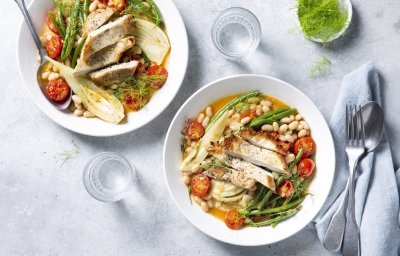 Bouillon met stukjes groenten en varkensvlees. De tomaten en boontjes zorgen voor een mooi kleurrijk bordje. De soep is uitgeschonken in twee diepe witte borden.  