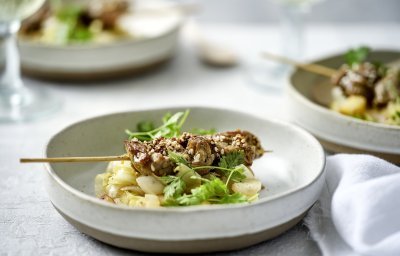 Er staan verschillende aperetiefbordjes op tafel met een schepje gestoofd witloof en appel. Hierop ligt een klein brochette van rundvlees en afgewerkt met kervel. 