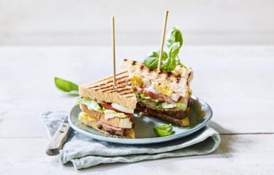 Goedgevulde club sandwich met lamsvlees en rauwkost. Gepresenteerd op een bord met middenin een prikker, klaar om op te eten. 