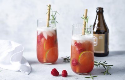 2 cocktails staan uitgeschonken in grote glazen. Deze cocktail op basis van bier en gin werd afgewerkt met frambozen en rozemarijn.