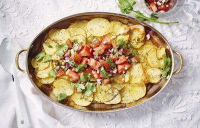 Aardappelschijfjes liggen gestapeld in een kopere ovenschaal. Hierop is de rode tomatensalsa geschept dat een mooi beeld geven tov het goudgele van de gegrilde patatjes. Her gerechtje is afgewerkt met korianderblaadjes. 