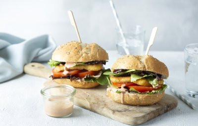 Een heerlijke hamburger die niemand koud laat. We maakten hem extra crunchy door de kaas te paneren alvorens hem te bakken. De twee hamburgers liggen op een houten snijplank met een prikker middendoor. 