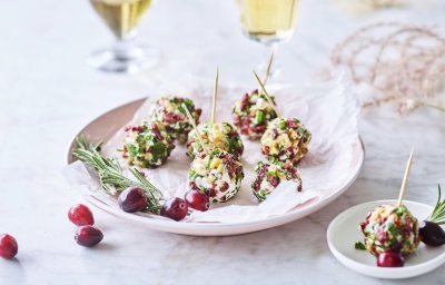 Kruidige kaasballetjes liggen op een licht roos bordje. Op de achtergrond staan 2 glaasjes aperitief met enkele veenbessen ter versiering. 