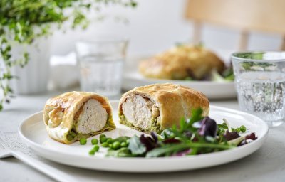 Een mini wellington van kipfilet ligt opengesneden op een wit bord. Hierin zie je mooi een laagje erwtjespuree onder het witte vlees in het bladerdeeg pakje. Er is nog wat gemengde sla en erwtjes toegevoegd op het bord. 