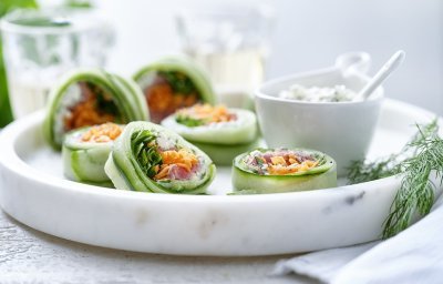 Rolletjes van komkommer gevuld met cottage cheese, wortel, rucola en rosbief. Een heerlijke gezonde en kleurrijke snack op een bordje van marmer. De overige mengeling met de cheese is geserveerd in een dippotje om eventueel een extra toefje te nemen. 