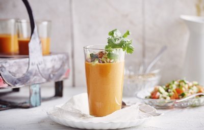 Een gazpacho van paprika geserveerd in een groot glas zorgt intens voor een feestlook. Deze koude soep werd gepimpt met stukjes komkommer en tomaat, als afwerking nog enkele blaadjes koriander en zonnebloempitten bovenop. 