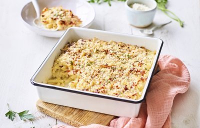 Een heerlijke gevulde ovenschotel boordevol comfortfood staat op de tafel te blinken. Onze mac and cheese met Belgische kazen zit in een witte ovenschotel met donker blauw randje, zoals bij de bomma. Er ligt een zalmroze servette langs en de een takje verse peterselie voor extra kleur in het beeld. 