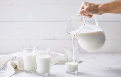 2 glazen zijn al gevuld met melk. Glazen kan met melk vult nog een glas. Glazen melk staan op marmere keukenaanrecht met linnen handdoek.