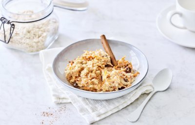 Een heerlijk ontbijtje dat smaakt naar worteltaart, dat kan je niet weerstaan! De overnight oats is geserveerd in een licht grijs diep bord, witte lepel langs en een kop verse koffie. Helemaal klaar om wakker te worden. 