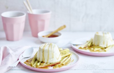 Een streling voor het oog, deze panna cotta met rabarber. Hij is opgediend in pastelroze bordjes en staat op een witte houten tafel. 