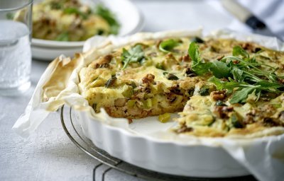 Een heerlijke quiche vers gebakken in een witte porseleinen taartvorm. Hij is gemaakt met spruitjes, champignons en prei. We voegden nog wat walnoten toe voor een extra bite. 