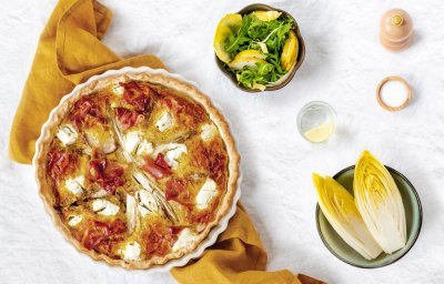 Een ronde quiche met wiltoof staat op een okkerkleurige handdoek op het aanrecht.