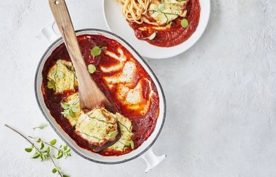 Pakjes van courgette liggen in witte ovenschaal met blauw randje. De tomatensaus ligt onder de ravioli van courgette, waardoor deze goed herkenbaar zijn. Er werd net een portie uitgeschept om meteen te eten. 