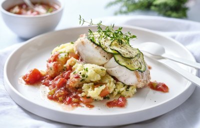 Roodbaars met schijfjes courgette erop, wachtend op een bedje van smeuïge puree en homemade tomtatensaus om eenvoudig te genieten. Achterin staat nog wat extra saus en verse kruiden. 