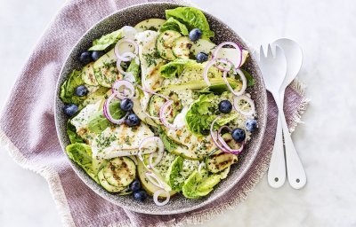 Een diep bord gevuld met sla, gegrilde zeetong, courgette, peer en blauwe bessen. Onder het bord ligt een paars servette en wit bestek om meteen dit gerechtje te verorberen. 