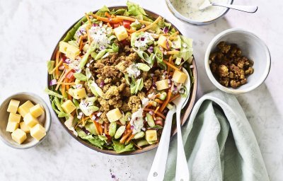 Een grote salade kom staat op het aanrecht, hij is gevuld met gemengde sla, komkommer, tomaten, worteltjes, stukjes kaas en gebakken gehakt. We werkte de salade af met een ranchdressing op basis van zure room en verse kruiden.
