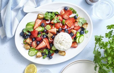 Er staat een grote schaal op tafel boordevol zomerse toppers. Denk maar aan tomaatjes, aardbeien, bosbessen, komkommers en burrata. Dit geeft echt verfrissing tijdens een zwoele zomerdag. Er ligt een citroentje langs, een glas water en verse kroiander.