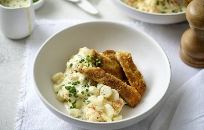 Handgeklopte schnitzel met wortelpuree en schorseneren liggen te blinken in een bordje. De mosterdsaus zit in een sauskannetje en kan je zelf toedienen naar eigen goesting. 