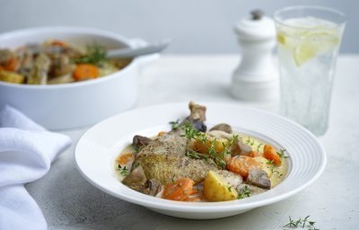 Een witte stoofpot staat op tafel. Deze keer is het eentje met kip, aardappelen en groentjes die gegaard zijn in melk. Er staat ook een glas water langs met een schijfje citroen. 