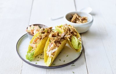Krokante taco's liggen op een bordje, ze zijn gevuld met stukjes varkensvlees en een slaatje van kool. 