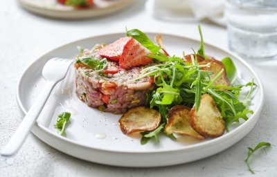 Zoek je een alternatief voor steak-tartaar? Wel dit is een zomerversie, nl eentje met kalfsvlees, aardbeien, tomaatjes en verse kruiden. We werkten het gerechtje af met gebakken aardappelplakjes en verse rucola. Er ligt een wit vork en servette naast om meteen aan te vallen. 