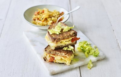 Een heerlijke cheesy toast ligt op een marmere snijplank. De toast is gevuld met 2 Belgische kazen, kimchi en chilisaus. 