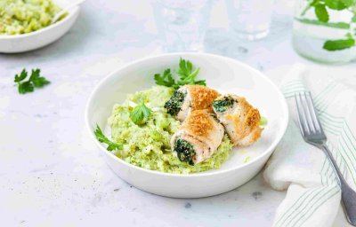 Gevulde tongrolletjes met spinazie en ricotta liggen op een groene puree van broccoli en aardappel. Ze liggen in een diep bord waarbij een karaf- en waterglas langs staat.