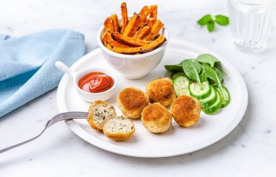 Visballetjes van wijting liggen op een wit bord met frietjes van pompoen erbij. Er staat ook een potje ketchup langs en een lichtblauwe servette. 