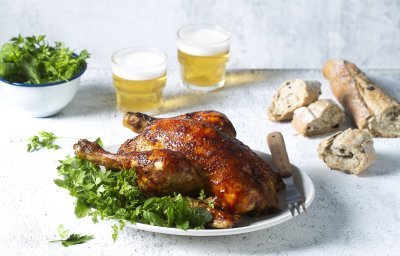 Een volledige kip op de BBQ op een blikje bier klaargemaakt, dit noemen we canned chicken. Deze kip kreeg een kruidige jas aan door de BBQ-saus. Ze ligt op een kruidige salade klaar om te knippen in stukken en op te peuzelen. 