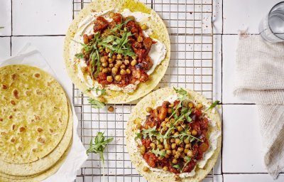 Twee wraps liggen op een ovenrooster klaargemaakt. Ze zijn belegd met roomkaas, tomatenspread en geroosterde kikkererwten. Er liggen nog enkele extra wraps langs. Het gerechtje is afgewerkt met enkele blaadjes rucola.