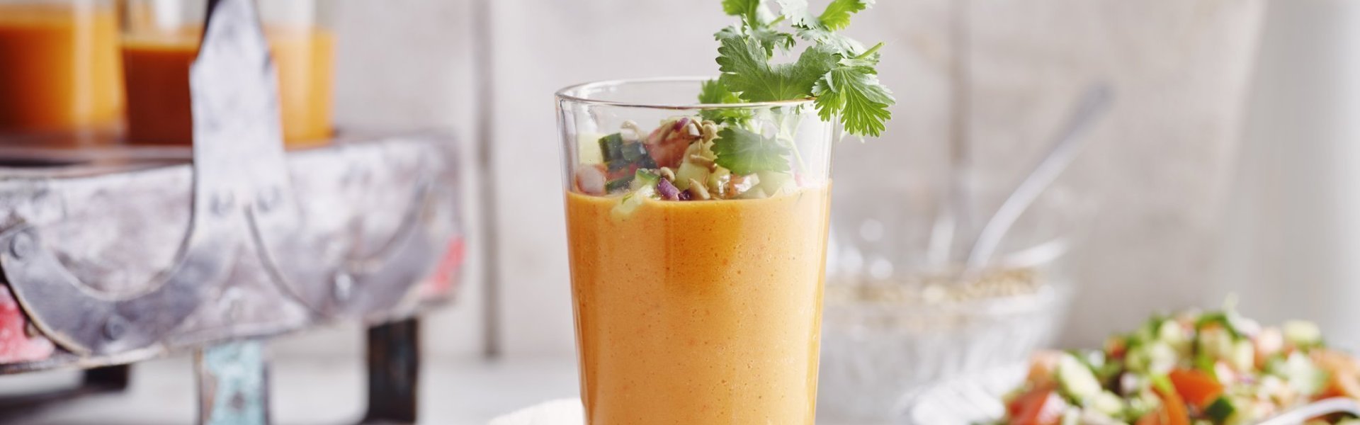 Een gazpacho van paprika geserveerd in een groot glas zorgt intens voor een feestlook. Deze koude soep werd gepimpt met stukjes komkommer en tomaat, als afwerking nog enkele blaadjes koriander en zonnebloempitten bovenop. 