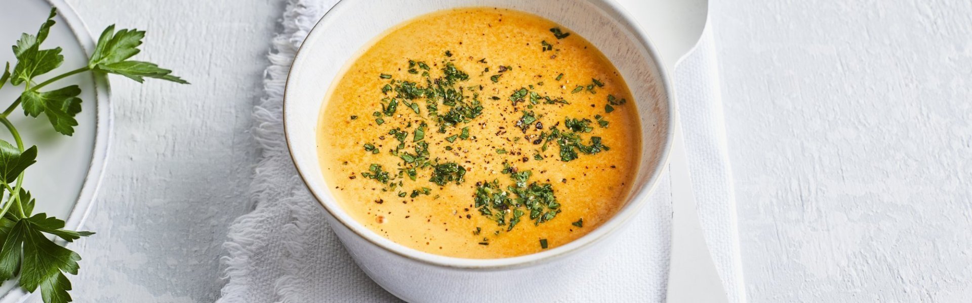 Paprikasaus Deze paprikasaus zit een wit kommetje wat een mooi contrast geeft met de oranje kleur van de saus. Er ligt een witte lepel langs en de saus is afgewerkt met verse groene kruiden.