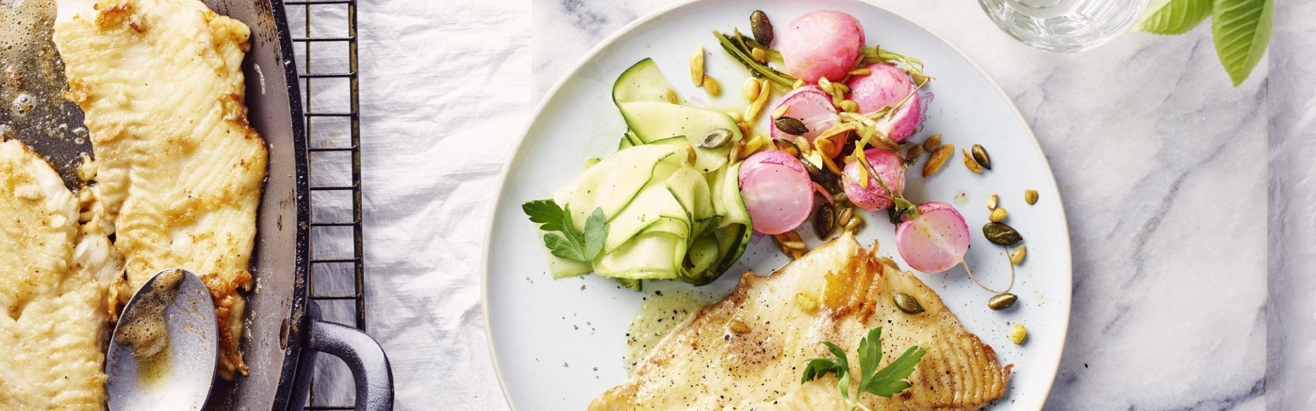Pladijsfilet met radijzen uit de oven en gemarineerde courgette Een rond bord is gevuld met het gerechtje. De grote ovenschaal staat op tafel met al een portie uitgeschept. De radijsjes zitten in een ander ovenschaaltje en staan eveneens op tafel. De radijsjes en courgette zorgen voor een mooie kleur in het gerechtje bij de vis.