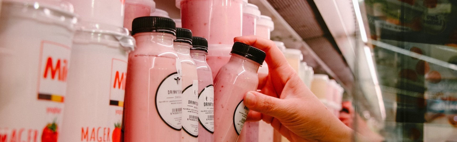 Carrefour Herent Zuivelrayon in Carrefour Herent, met drinkyoghurt van lokale handelaar. De consument neemt een drinkyoghurt met aardbeiensmaak uit het koelschap.